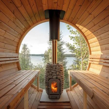 Barrel sauna interior with opposing cedar benches and wood-burning heater facing a lake
